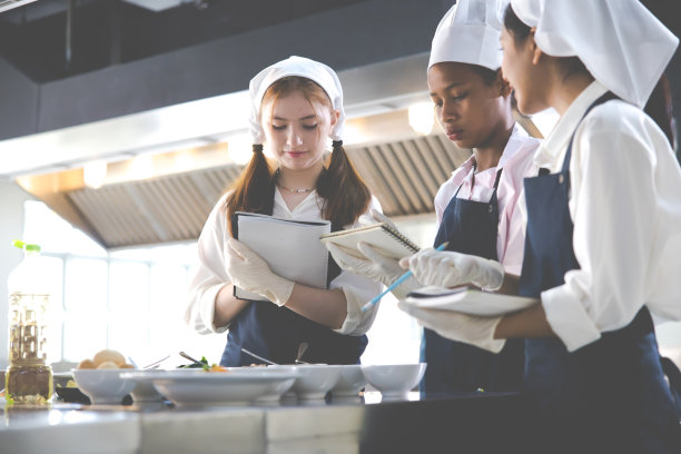 记在本子上。烹饪课。烹饪教室。一群快乐的多民族女学生正在烹饪学校学习烹饪课程。图片下载
