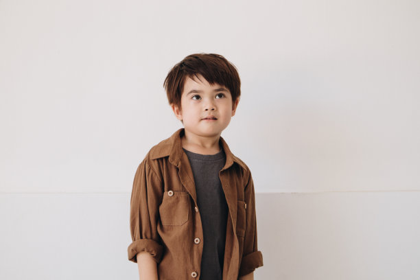 一个男孩的肖像，穿着一件棕色的彬彬有礼的衬衫，露出一副若有所思的表情。图片下载
