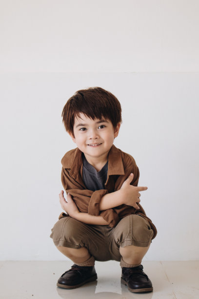 一个男孩的肖像，穿着一件棕色的彬彬有礼的衬衫，蹲着，交叉着双臂。图片下载