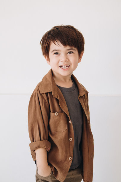 一个男孩的肖像，穿着一件棕色的正装衬衫，露出笑容，双手插在口袋里。图片下载