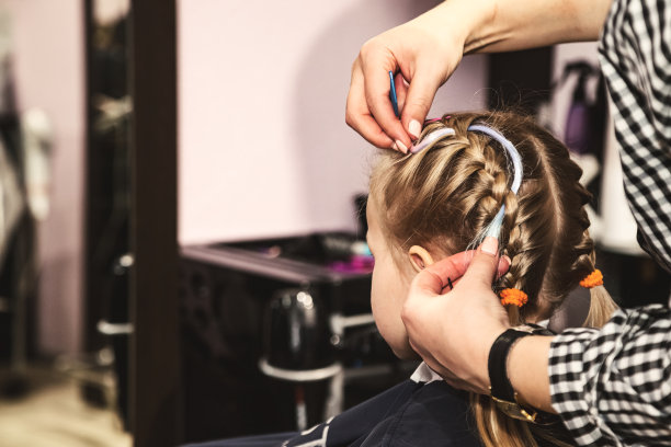理发师在理发店为小婴儿编发辫。在现代理发店，美发沙龙，女理发师为可爱的金发小女孩做发型。概念发型和美丽。复制广告文本空间图片下载