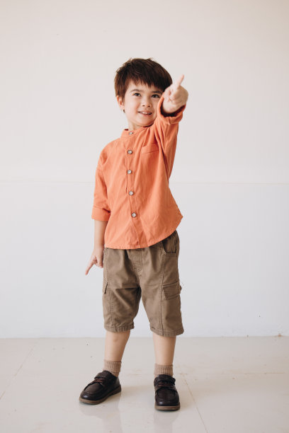 一个男孩的肖像，穿着一件彬彬有礼的橙色衬衫，手指着镜头摆姿势。图片下载