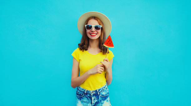 夏日肖像的快乐开朗的年轻女子与新鲜多汁的水果，棒棒糖或冰淇淋形状的西瓜片戴草帽，太阳镜在蓝色的背景图片下载