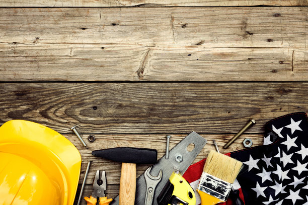 劳动节快乐横幅设计。框架边框由美国国旗，安全帽，木制背景上的木工工具制成。平躺，俯视图。图片下载