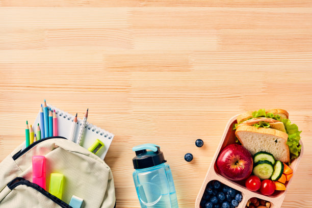 健康儿童午餐盒和书包，木桌上有学习用品。前视图。平的。图片下载