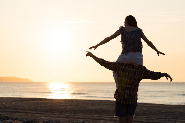 一对夫妇在海滩上欣赏日落。一对情侣在沙滩上欣赏浪漫的日落图片下载