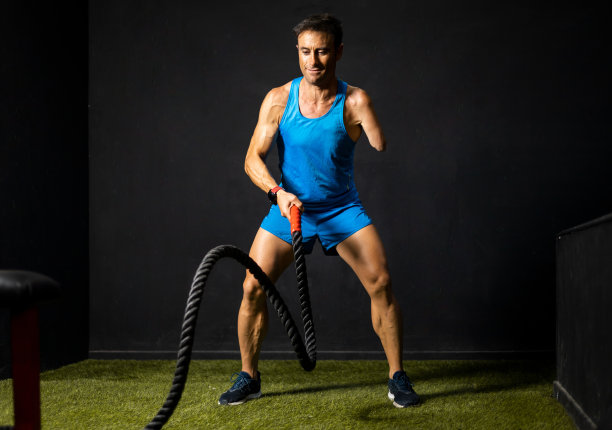 一个被截肢的成年运动员在健身房里做战斗绳练习的横向照片。战斗绳概念，残疾健美运动员，被截肢的运动员。改进。图片下载