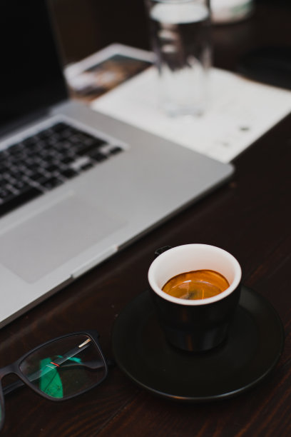 现代的工作场所，笔记本电脑，一杯新鲜的咖啡，一杯水和木桌上的玻璃杯图片下载