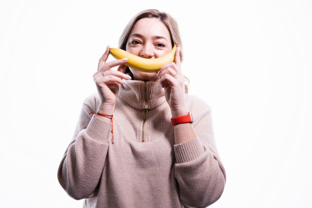 可爱的女人的肖像，孤立的拿着香蕉在她的嘴，而不是嘴唇，微笑，有乐趣，心情很好，表达积极的情绪图片下载