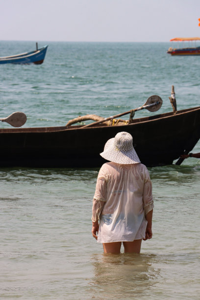 难以辨认的特写照片，白人妇女站在大腿深的海水中，穿着防晒服，戴着松软的遮阳帽，遮住太阳，游船在潮汐中漂浮，这是后视图图片下载