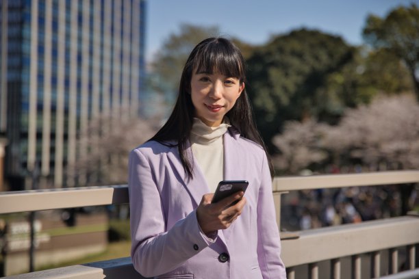 一名日本女子在樱花后面拿着智能手机图片下载
