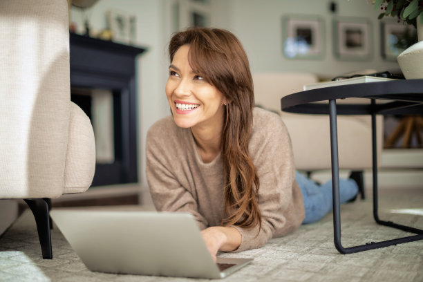 迷人的中年女人躺在现代家庭的地板上，用笔记本电脑工作图片下载