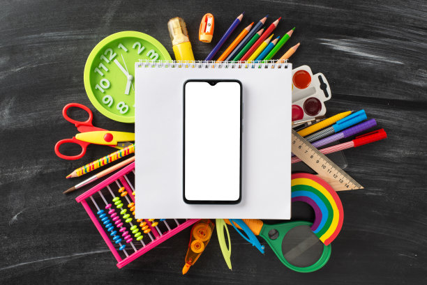 用这个创意自上而下的图像进入学习的世界:一个令人愉快的儿童文具分类，围绕笔记本页面排列，智能手机在黑板孤立的背景上图片下载