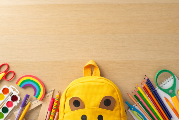 教室布置。各种工具的顶视图，相册，绘画集，彩色铅笔，尺子，放大镜，好玩的熊袋，彩虹橡皮泥木制桌面背景与文字的空间图片下载
