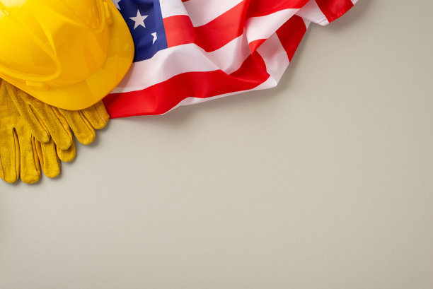 以建筑为主题的劳动节庆祝活动:用这个迷人的自上而下的快照点燃兴趣，在浅灰色的背景下，有国旗，工作头盔，手套。理想的劳动节促销或广告图片下载