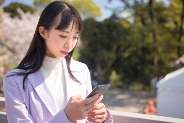 一名日本女子在樱花后面使用智能手机的肖像图片下载