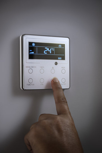 一只手调节恒温器的温度。图片下载