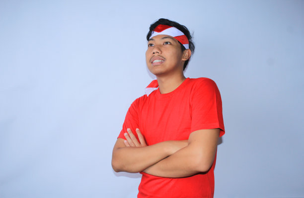 图为，为庆祝印尼独立日，身穿红色t恤，头戴头巾，双手交叉微笑的一名印尼青年，目光转向别处图片下载