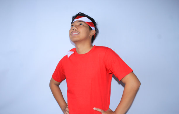 图为，为庆祝印尼独立纪念日，身穿红色t恤、头带的一名印尼青年正双手叉腰微笑着望向别处图片下载