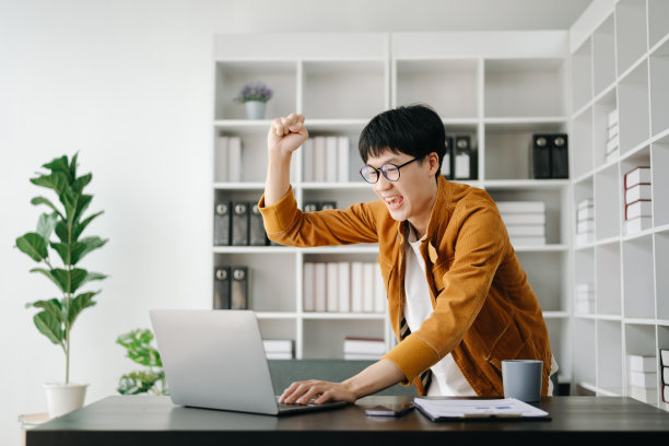 亚洲商人对他们在办公室用平板电脑、笔记本电脑和做笔记所做的工作感到高兴和快乐。图片下载