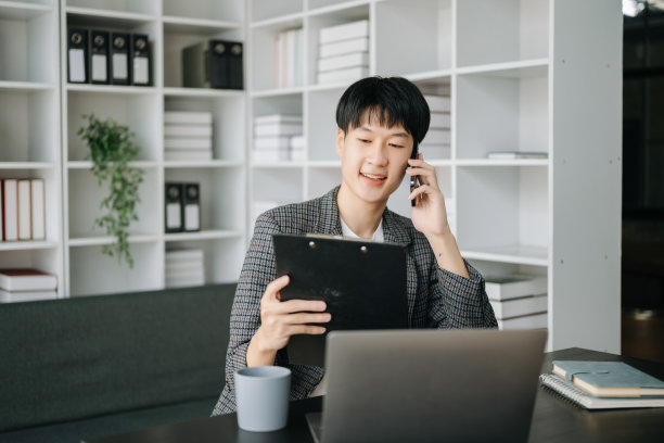 年轻的商人在现代办公室工作，用笔记本电脑，平板电脑和在纸上做笔记。图片下载