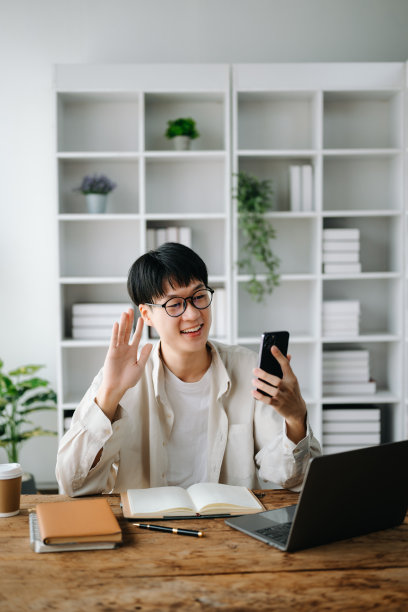 迷人快乐的年轻亚洲学生在大学图书馆学习，坐在桌子前，使用笔记本电脑，平板电脑和耳机进行视频聊天。图片下载