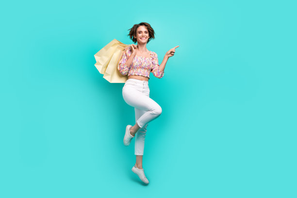 全尺寸照片华丽兴奋的女孩跳hold精品包表明手指空白空间孤立在蓝绿色的背景图片下载