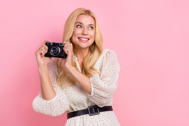 卷发的形象专业摄影师女孩的业余爱好视频相机抓拍回忆她的旅行孤立的粉红色背景图片下载