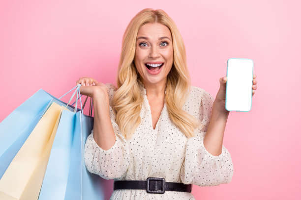 迷人的金发女人的照片肖像购物袋显示白色空白屏幕穿时髦的白色衣服孤立在粉红色的背景图片下载