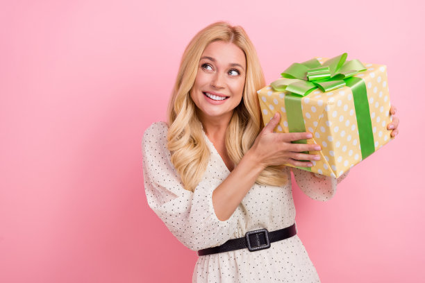 迷人的金发女子的照片肖像拿着礼物盒看空空间穿着时尚的白色衣服孤立在粉红色的背景图片下载