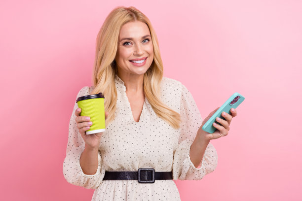 照片肖像迷人的金发女子手持纸杯咖啡装置穿着时尚的白色衣服孤立在粉红色的背景图片下载