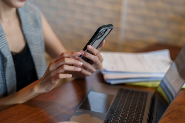 年轻的亚洲女商人手持智能手机的特写镜头。桌子上有一台笔记本电脑。在工作时间内。通过智能手机讨论工作。图片下载
