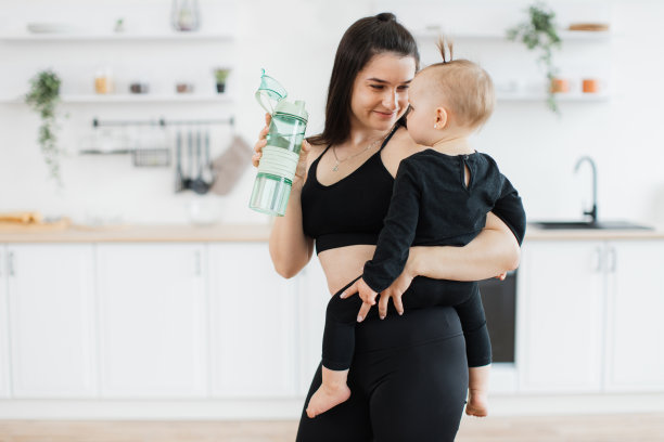 妈妈拿着运动瓶在家里对着怀里的孩子微笑图片下载