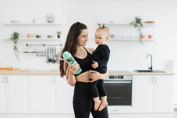 妈妈拿着运动瓶在家里对着怀里的孩子微笑图片下载