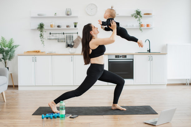 女士把孩子抱成飞机姿势，在垫子上伸展身体图片下载