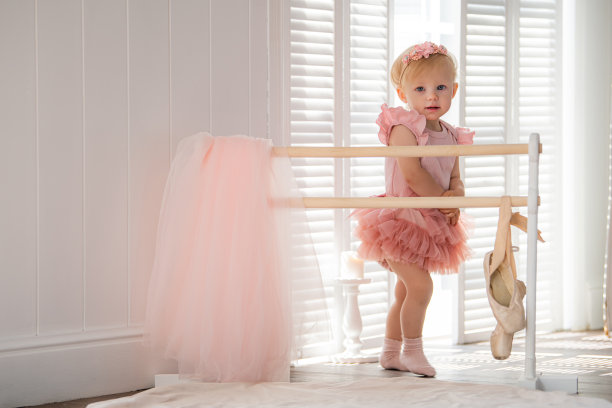 一个穿着粉红色芭蕾舞服的可爱的小芭蕾舞女演员站在房间里的芭蕾舞杠旁边。孩子和芭蕾舞。Copyspace。图片下载