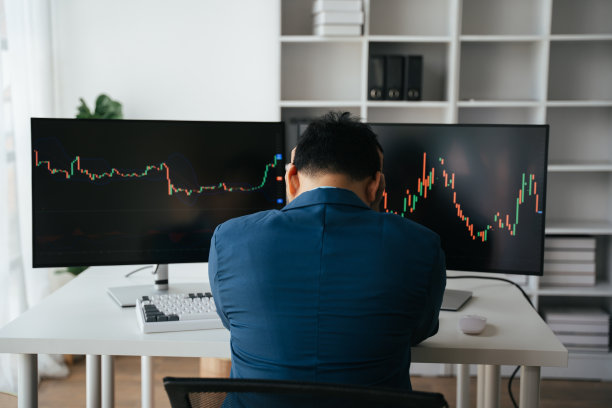 年轻的商人双手捂着脸坐在创意办公室的办公桌前，股票市场的概念。图片下载