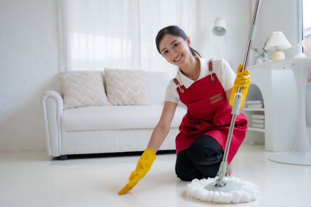 快乐的亚洲年轻女子正在拖地。戴着手套、系着围裙的亚洲主妇正在愉快地打扫房间。图片下载