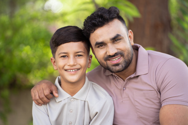 幸福微笑的印度父亲和儿子在公园里看着镜头互相拥抱——家庭团聚、世代和父亲的概念。图片下载