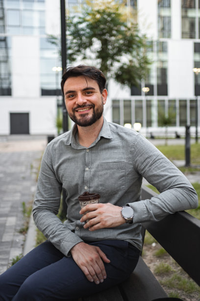 一个成熟的白人男子坐在工作大楼前的长椅上喝咖啡图片下载