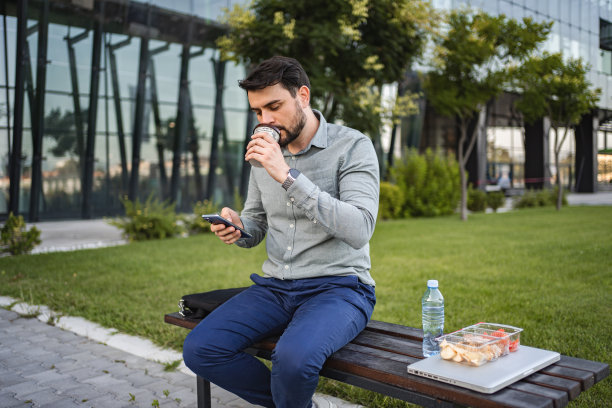 白人商人坐在公园长椅上喝咖啡时发短信图片下载