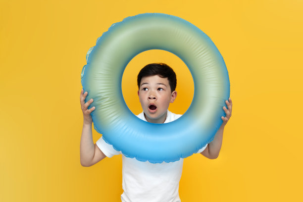 小亚洲男孩拿着充气游泳圈，惊讶地看着黄色背景图片下载