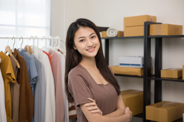 年轻美丽的亚洲女性企业主在时尚商店检查库存轨道服装站和微笑对相机。在服装店工作的亚洲女性企业家。图片下载