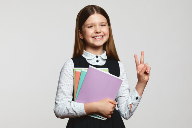 高兴的小学生穿着校服，拿着课本，对着白人做着和平的手势图片下载