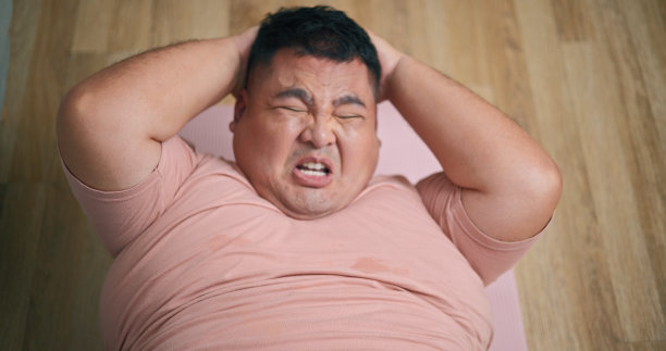 小胖子在客厅木地板上做仰卧起坐练习图片下载