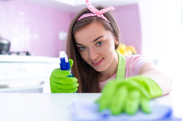 年轻的家庭主妇戴着防护橡胶手套，在厨房里用抹布和喷雾近距离擦拭灰尘。春季大扫除图片下载
