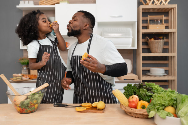 快乐的非裔美国小女孩在家和爸爸一起在厨房做沙拉图片下载
