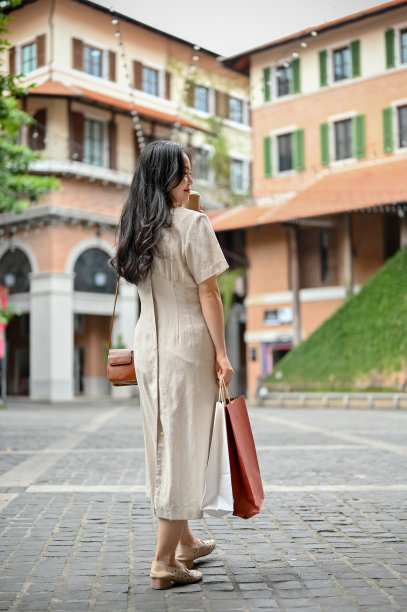 一个迷人的亚洲女人在一个漂亮的衣服漫步在美丽的城市独自在她的假期。图片下载