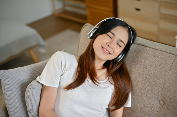 一位年轻漂亮的亚洲女子躺在沙发上放松地听着耳机里的音乐图片下载