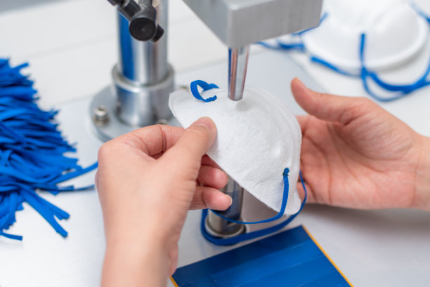 这个女孩在一家生产医用口罩的工厂工作，用纳米纤维和超声波在机器上焊接线圈。冠状病毒和Covid-19防护特写图片下载